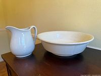 White ironstone pitcher and matching bowl on dark surface against beige wall