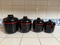 Front view of four black and red lacquered Japanese lidded pots arranged from largest to smallest.