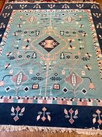 Full view of rug laid flat on hardwood floor showing turquoise center field with multicolor geometric and floral patterns and navy border.