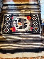 Full view of the large rectangular wool rug showing central bird pictorial design and geometric surrounding patterns in black, white, brown, red, and orange colors.