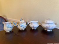 Four porcelain pieces including two small creamers and two covered sugar bowls with floral designs and gold trim.