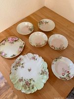 Seven vintage Limoges Haviland berry bowls displayed on a wooden surface, showing floral patterns and shapes.
