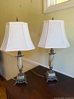 Pair of vintage table lamps on a wooden surface, featuring marble shafts and white lampshades.