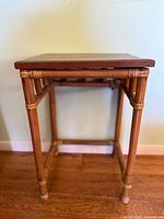 Front view of bamboo side table with wooden top on wood floor against light wall
