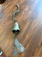 Photo of the entire bronze bell wind chime laid flat showing the bell, clapper, pendant, and twisted hanger.
