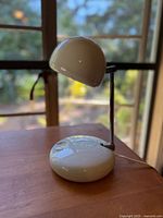 Off-white vintage Tensor eyeball desk lamp with telescoping arm on wooden surface near window, showing side profile and base details.