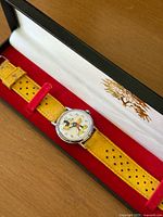 Front view of vintage Mickey Mouse watch in box showing dial with Mickey figure and yellow perforated leather strap.