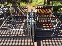 Two mid-century style aluminum chairs with redwood slatted seats and backs, placed side by side under dappled sunlight.