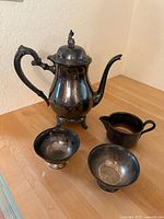 Full view of the coffee set including coffee pot with lid, creamer, and two small dishes on wooden surface.