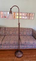 Full view of copper tone bridge floor lamp standing next to floral-patterned couch on hardwood floor