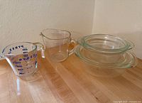 Photo showing two clear Pyrex glass mixing bowls stacked and two glass measuring cups, one Pyrex branded with blue measurements and one smaller clear pitcher with red markings.