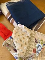 Close-up of stacked scarves showing beige scarf with hand rolled edge tag reading 'Pure Silk' with star pattern and Southwestern style design under blue scarf.