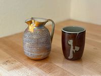 Photo showing vintage Stangl creamer with gold accents and Japanese ceramic cup side by side on wooden table.