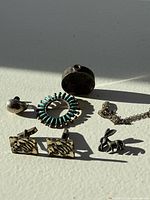 Photo showing all items including teardrop pin, turquoise circle pin, round locket pendant, cufflinks, rabbit pin, and chain