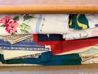 Photo showing a collection of folded vintage textiles stored inside a wooden drawer. Textiles vary in design, color and pattern including florals, stripes, solid fabrics, and geometric prints.