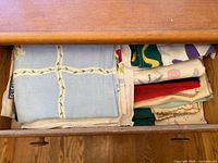 Top view of a wooden drawer containing folded vintage textile pieces with varied patterns and colors.