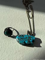 Vintage turquoise ring and pendant jewelry on white surface with shadows, showing details of stones and metalwork