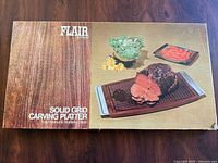 Original box for Flair solid walnut wood carving platter showing product name and serving suggestion with meat and vegetables.