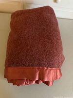 Folded vintage wool blanket with coral/orange satin trim on edges.