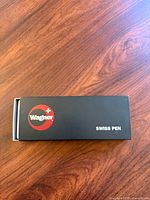 Photo showing the sealed black Wagner Swiss Pen box on wooden surface, with red and white logo.