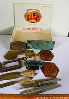 Group shot of all items with open cigar box, knives, brass pieces, marble block and plaques
