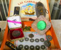 Open cigar box showing coins, jade rests, metal frame, coin pendant, display card