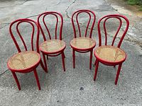 Four red bentwood chairs with cane seats displayed outdoors
