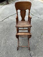 Front view showing full high chair, cane seat, footrest, and wheels
