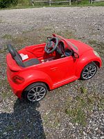 Red ride-on VW Beetle side profile showing wheels, interior, steering wheel