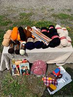 Entire lot on table showing yarn skeins, pattern books, needles, yarn bowl, fabric panel