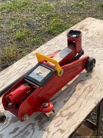 Full view of red hydraulic floor jack on wooden surface