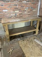 Full view of hardwood workbench against brick wall showing top, legs, and shelf