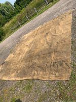 Full view of large brown canvas tarp laid out on gravel