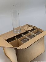 Closed box with partitioned interior holding 11 glasses plus one glass standing outside