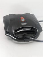 Closed waffle maker showing top housing with indicator lights and handle