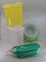 group shot of yellow and white rectangular containers, green ring mold with lid, and green perforated accessory