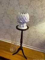 white ceramic vase on dark wood stand beside clear glass vase