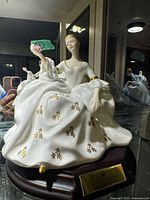 Front view of figurine on wooden base showing lady, rose, gown and brass plaque