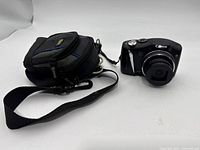 Camera front angled view showing lens, controls, wrist strap, and carrying pouch