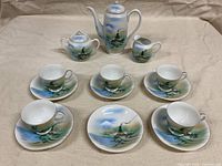 Full 14-piece tea set arranged showing hand painted landscape design
