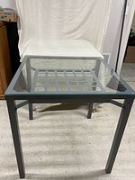 Front view of square gray metal table with glass top
