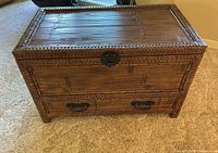 Front view of the rattan storage chest showing top lid, front panel and lower drawer with metal pulls