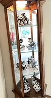 Full view of walnut glass corner cabinet with multiple penguin figurines on glass shelves