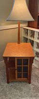 Maple finish side table with attached lamp, cabinet door visible
