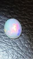 Oval cabochon opal showing red and green flash on dark textured background