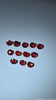 Top view of 12 natural round rubies on white background, showing red color and round faceting.
