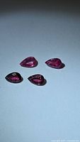 Four pear-shaped sapphires in hot pink and purple displayed on a flat surface under direct light.