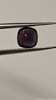 Front view of cushion cut purple spinel gemstone held by tweezers showing gem color and clarity