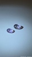 Two natural amethyst gemstones of light pink purple color, oval cut, displayed against a light background showing their clarity and faceting.