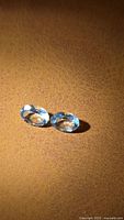 Pair of oval cut light blue aquamarine gemstones placed on a brown textured background, showing clarity and transparency.